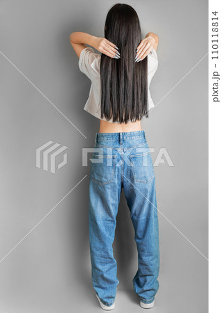 The girl stands with her back to the camera and straightens her long dark hair. 110118814
