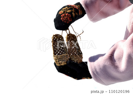 Hands with black mittens with russian traditional pattern holding bast shoes isolated on white background 110120196
