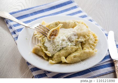 cooked dumplings with meat, spices and sour cream, in a plate on a light wooden table. 110121890