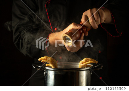 The chef adds pepper to a pot of boiling chicken legs. Concept of preparing a delicious side dish in a restaurant or hotel kitchen 110123509