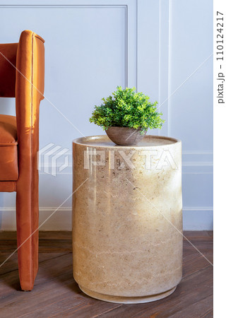 Potted plant on marble table by chair in living room. Table has round top and pedestal base 110124217