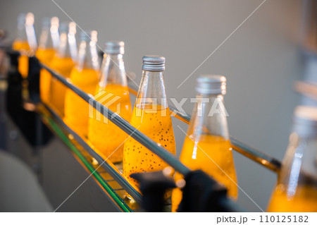 Bottling factory's efficient line fills transparent bottles with organic basil or chia seed drinks mixed with pomegranate. Automated clean technology ensures high-quality liquid production. 110125182