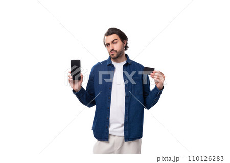 young european brutal brunette man with a cool hairstyle dressed in a denim shirt shows a phone young european brutal brunette man with a cool hairstyle dressed in a denim shirt shows a phone 110126283