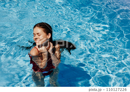 Happy woman swimming in the pool in red swimsuit with loose long hair in the sunshine, skin protection with sunscreen, concept of relaxing on vacation. 110127226