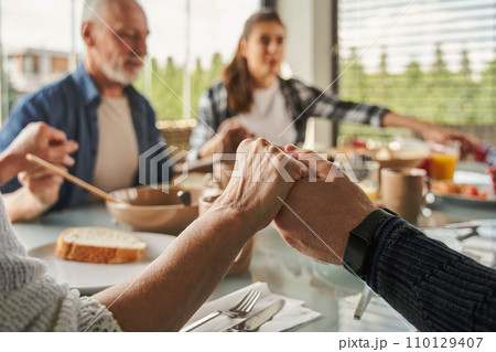 Christian family praying before breakfast and holding hands at the kitchen table 110129407