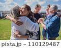 Smiling daughter embracing her senior mother while standing at the green grass lawn 110129487