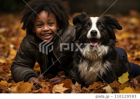 Energetic black boy having fun with his dog outdoors in the park in autumn 110129593