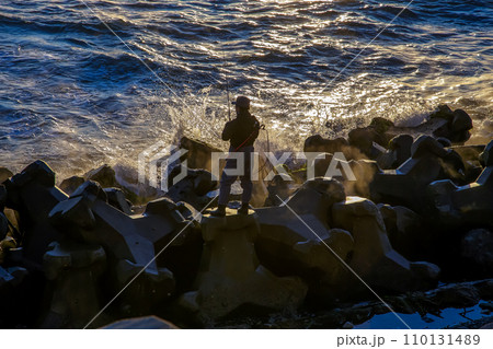 朝日の太陽光を浴びなが海に竿を垂らす釣り人 朝日の太陽光を浴びなが海に竿を垂らす釣り人 110131489