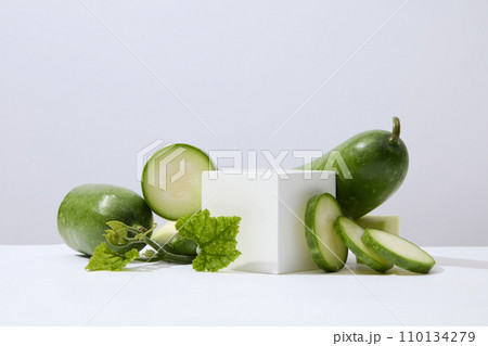A white cube placed on white surface with green leaves and winter melon slices. Glamour minimal pedestal for beauty, cosmetic product presentation A white cube placed on white surface with green leaves and winter melon slices. Glamour minimal pedestal for beauty, cosmetic product presentation 110134279