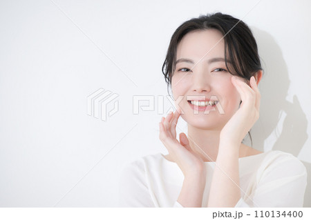 頬に手を当てスキンケアを実感して喜ぶカメラ目線の若い女性ビューティー 110134400