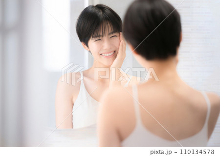 美容などのイメージで使いやすい洗面台で鏡を見る美しい女性のカメラ目線で頬を触る 110134578