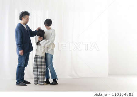 ママに抱きつく小学生娘と娘の頭を撫でるパパの3人家族全身広角 ママに抱きつく小学生娘と娘の頭を撫でるパパの3人家族全身広角 110134583