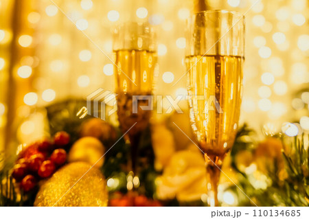 Two champagne glasses filled with champagne are placed on a table with a fruit arrangement. The glasses are surrounded by lights, creating a festive atmosphere. 110134685