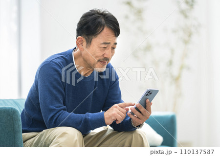 ソファに座ってスマートフォンを操作する50代の男性 110137587