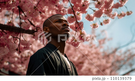 Modern happy young smiling dark-skinned African man against the backdrop of pink cherry blossoms  110139379