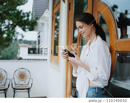 Woman on the balcony of the house with phone beautiful smile on a day off, beautiful view of nature in the mountains, lifestyle vacation in the hotel. 110140830