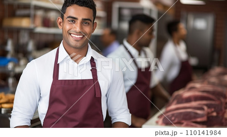 Smiling Young Butcher with Expertise, Assisting Customers at the Well-Stocked Meat Counter Smiling Young Butcher with Expertise, Assisting Customers at the Well-Stocked Meat Counter 110141984
