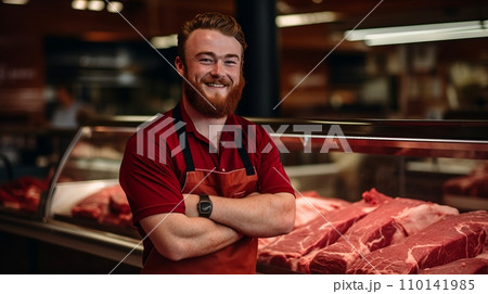 Friendly Butcher Standing at Well-Stocked Meat Counter with Fresh Cuts 110141985