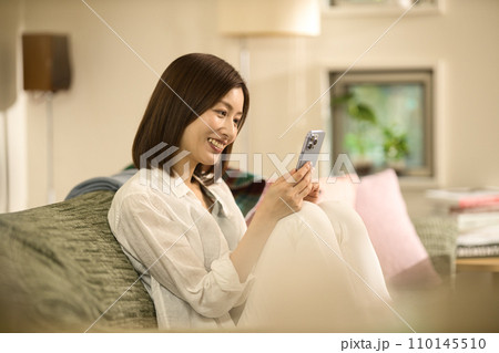 ソファーでくつろいでスマホを見るミドル女性 110145510