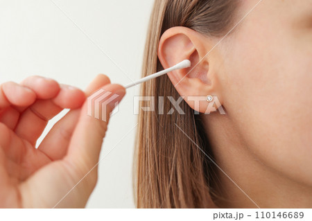 woman holds in hand disposable cotton bud, swab, stick. Girl cleans, washes her auricle earwax. Personal hygiene and care product. Prevention of ear diseases. Sulfur plug removal. 110146689