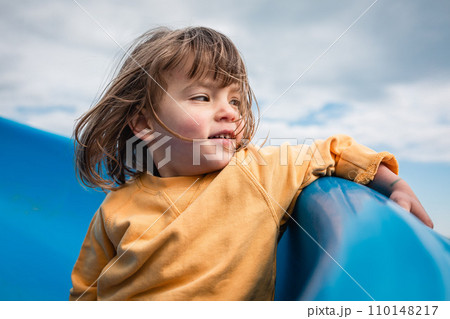 little girl in yellow clothes going down blue slide watching aside little girl in yellow clothes going down blue slide watching aside 110148217