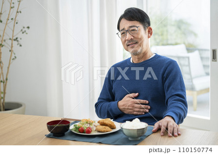 食卓でお腹に手を当てる50代半ばの男性 食卓でお腹に手を当てる50代半ばの男性 110150774