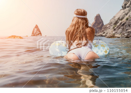 Woman summer sea. Happy woman swimming with inflatable donut on the beach in summer sunny day, surrounded by volcanic mountains. Summer vacation concept. 110155054