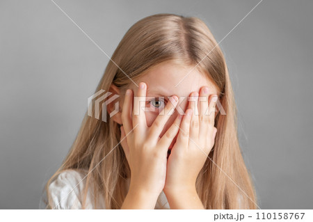 A little girl covering her face with her hands 110158767