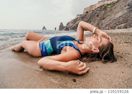 Woman summer travel sea. Happy tourist in blue bikini enjoy taking picture outdoors for memories. Woman traveler posing on the beach surrounded by volcanic mountains, sharing travel adventure journey 110159126