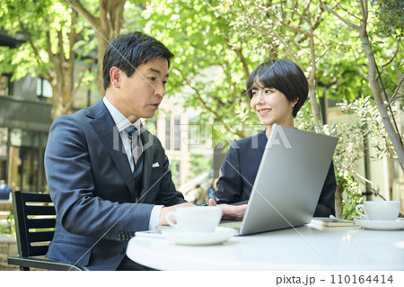 テラス席で打ち合わせをする50代男性会社員と30代女性会社員 テラス席で打ち合わせをする50代男性会社員と30代女性会社員 110164414