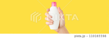 Womans hand holding white bottle on yellow background. Self care concept. Womans hand holding white bottle on yellow background. Self care concept. 110165598