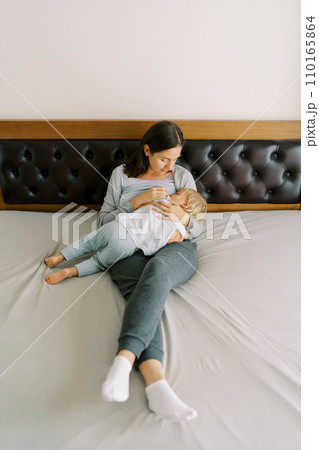 Mom breastfeeds a little girl, lying with her on the bed Mom breastfeeds a little girl, lying with her on the bed 110165864