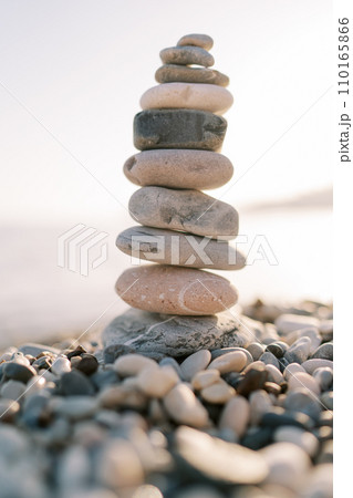 Cairn stands on a pebble beach in bright sunlight 110165866