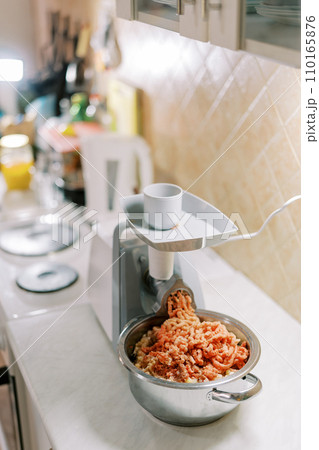Pot with minced meat is on the table in front of the electric meat grinder 110165876