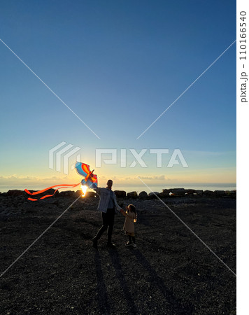 Mom with a little girl stands with a kite in her hands against the backdrop of sunset Mom with a little girl stands with a kite in her hands against the backdrop of sunset 110166540
