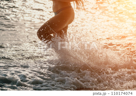 Running woman on a summer beach. A woman jogging on the beach at sunrise, with the soft light of the morning sun illuminating the sand and sea, evoking a sense of renewal, energy and health. Running woman on a summer beach. A woman jogging on the beach at sunrise, with the soft light of the morning sun illuminating the sand and sea, evoking a sense of renewal, energy and health. 110174074