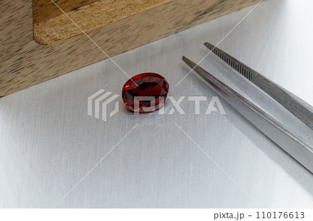 macro mineral faceted stone Garnet with tweezers on a gray background macro mineral faceted stone Garnet with tweezers on a gray background 110176613