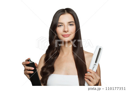 Pretty young adult woman using hair iron and straightening her long brown hair on white background Pretty young adult woman using hair iron and straightening her long brown hair on white background 110177351