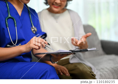 Healthcare worker pointing at clipboard showing health test results to senior patient during home visit. 110180235