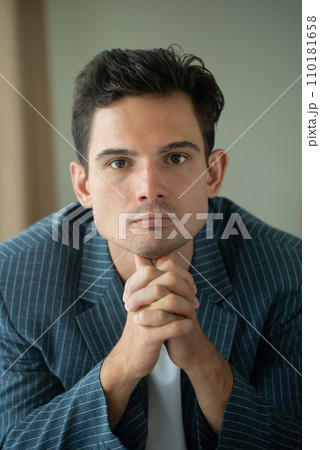 Close-up of young handsome guy in a white shirt, looks seriously and intently at the camera indoor 110181658