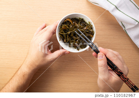 Man holding chopsticks with seaweed salad over bowl 110182967