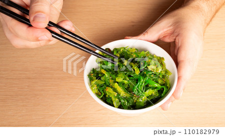 Man holding chopsticks with Japanese seaweed salad over bowl 110182979