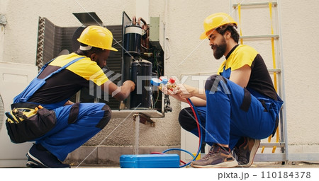 African american repairman cleaning condenser internal components of dirt while coworker assembles professional manifold meters to check freon levels in hvac system 110184378