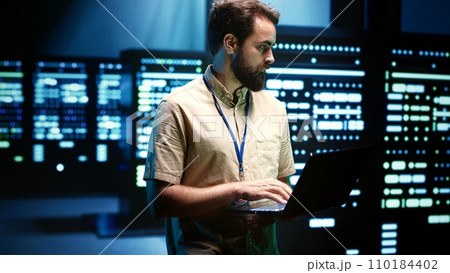 Close up of adept technician using laptop to check operational server hub. Hardware clusters in data storage and cloud computing business service providing processing for several workloads Close up of adept technician using laptop to check operational server hub. Hardware clusters in data storage and cloud computing business service providing processing for several workloads 110184402
