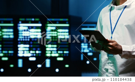 IT specialist walking through server rows performing data backups, close up. Serviceman using tablet to make sure electric generators are able to ensure operational continuity 110184438