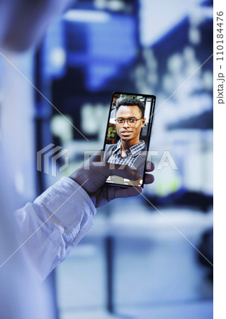 Woman in online videocall with husband while walking around city streets at night, close up. Citizen using phone for remote connection with spouse, showing him surroundings in urban center 110184476