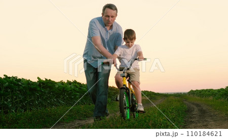 Father leads son biking among plantation on vocation at countryside at sunset 110184621