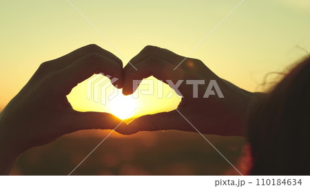 Hands of woman came to countryside to rest folded in shape of heart at sunset 110184634