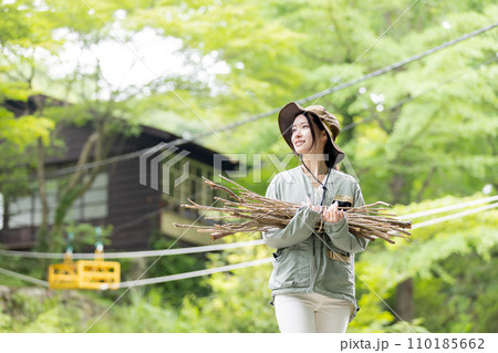 キャンプで薪(枝)を運ぶ女性 110185662
