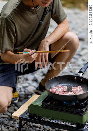 キャンプで豚肉を焼く男性　ガスコンロ 110185869